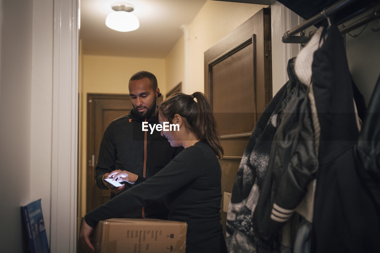 Female customer signing on mobile phone for delivery from male worker at doorway