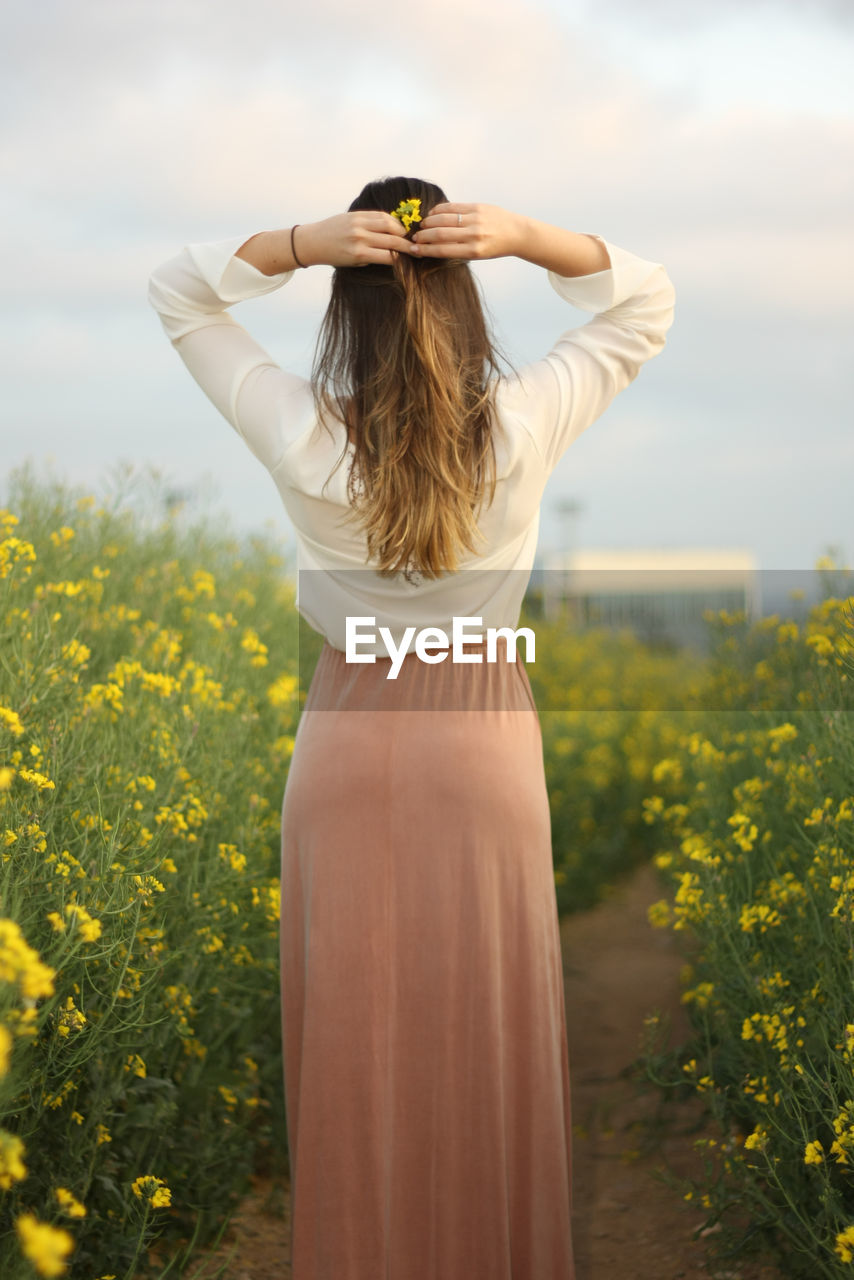 Rear view of woman standing by flowering plants against sky