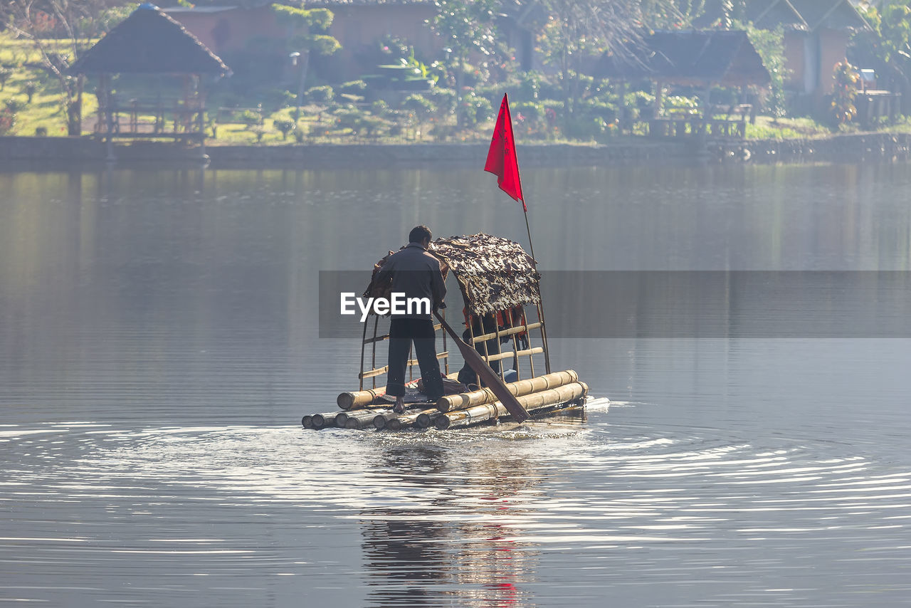 Rear view of man standing in wooden raft on lake