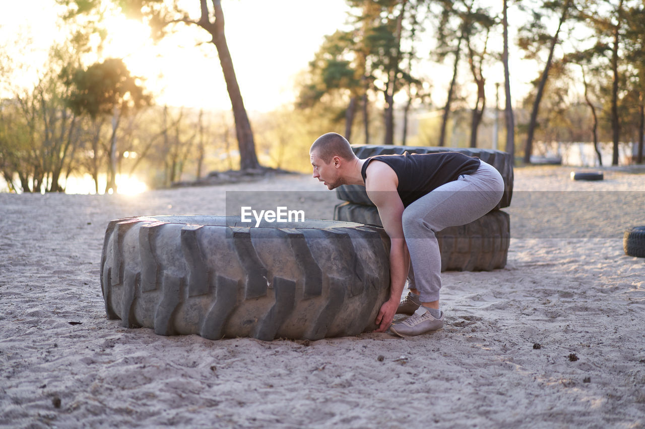 Full length of young man lying lifting tire outdoors