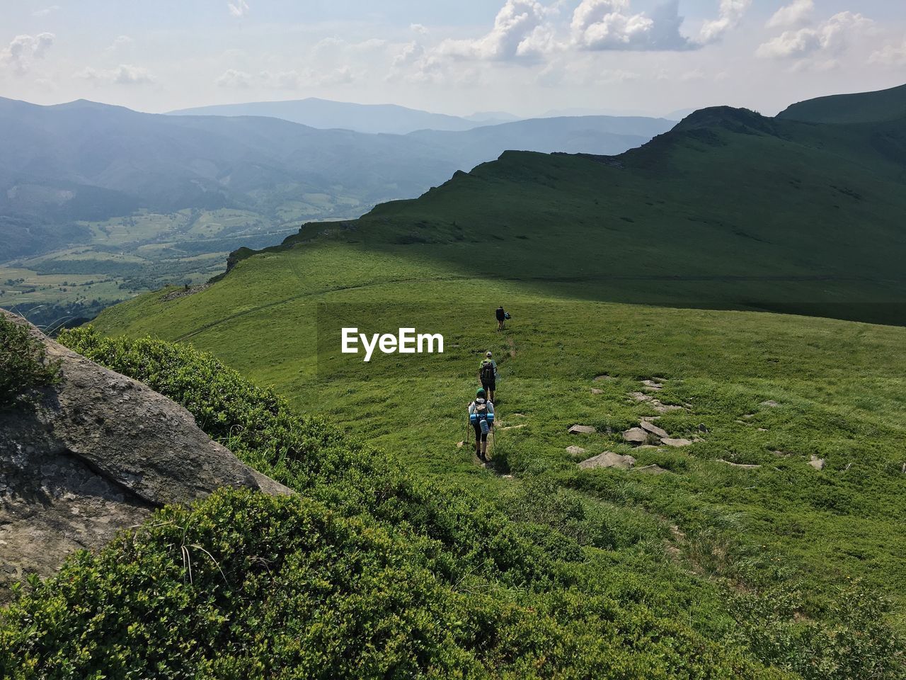 High angle view of people hiking on green mountains during sunny day