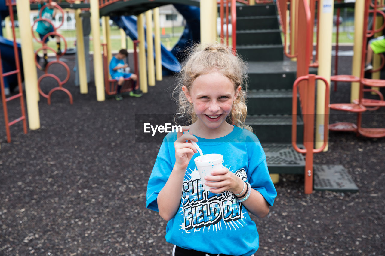 Smiling curly haired girl eats slush on school playground at field day