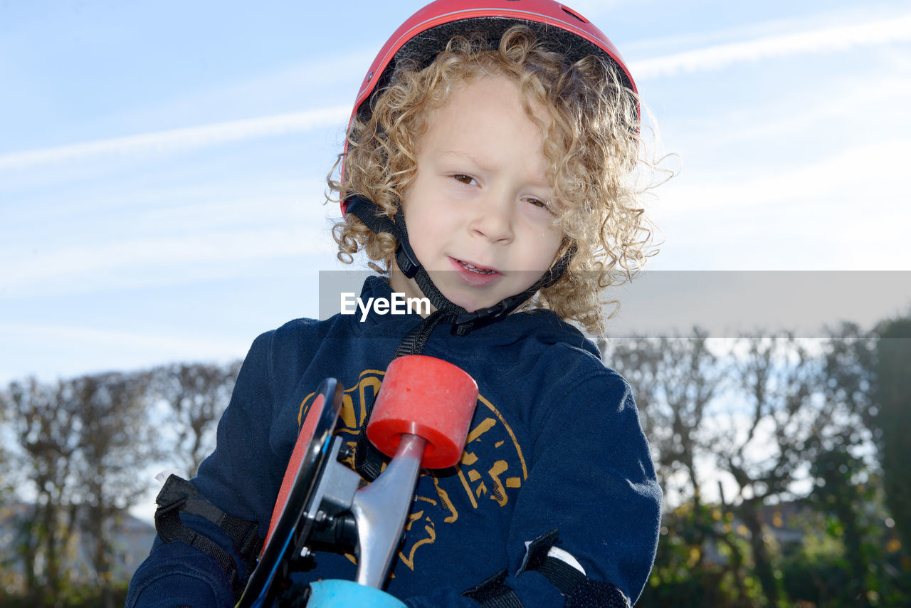 Portrait of cute boy holding skateboard standing against sky