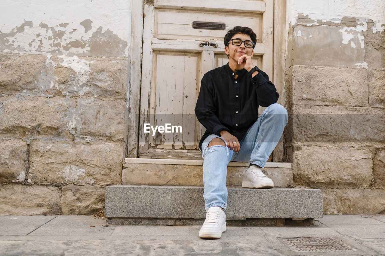 Young transgender man posing sitting on the front steps of a house.