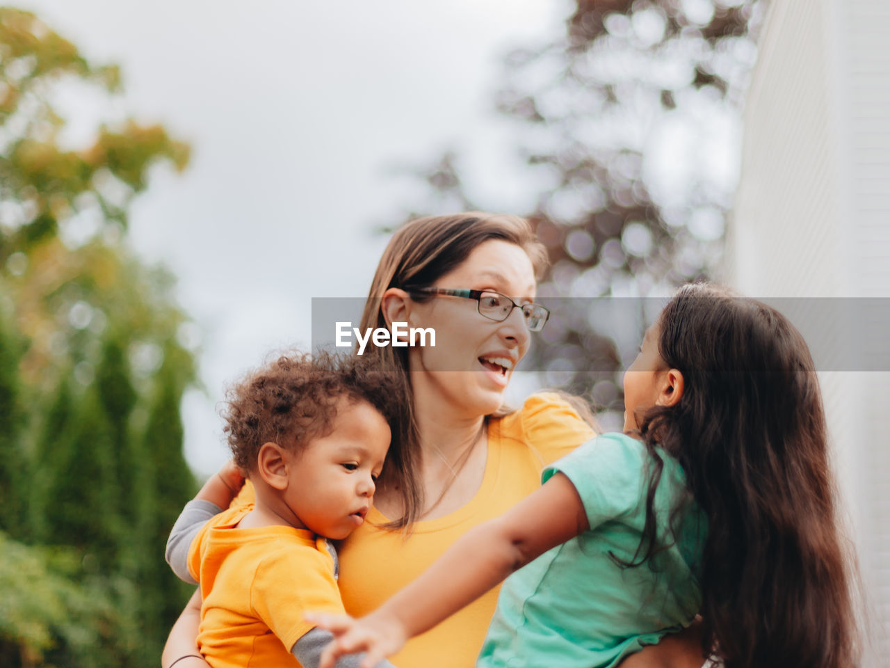 Young millennial mother at home playing with her two mixed race children in backyard