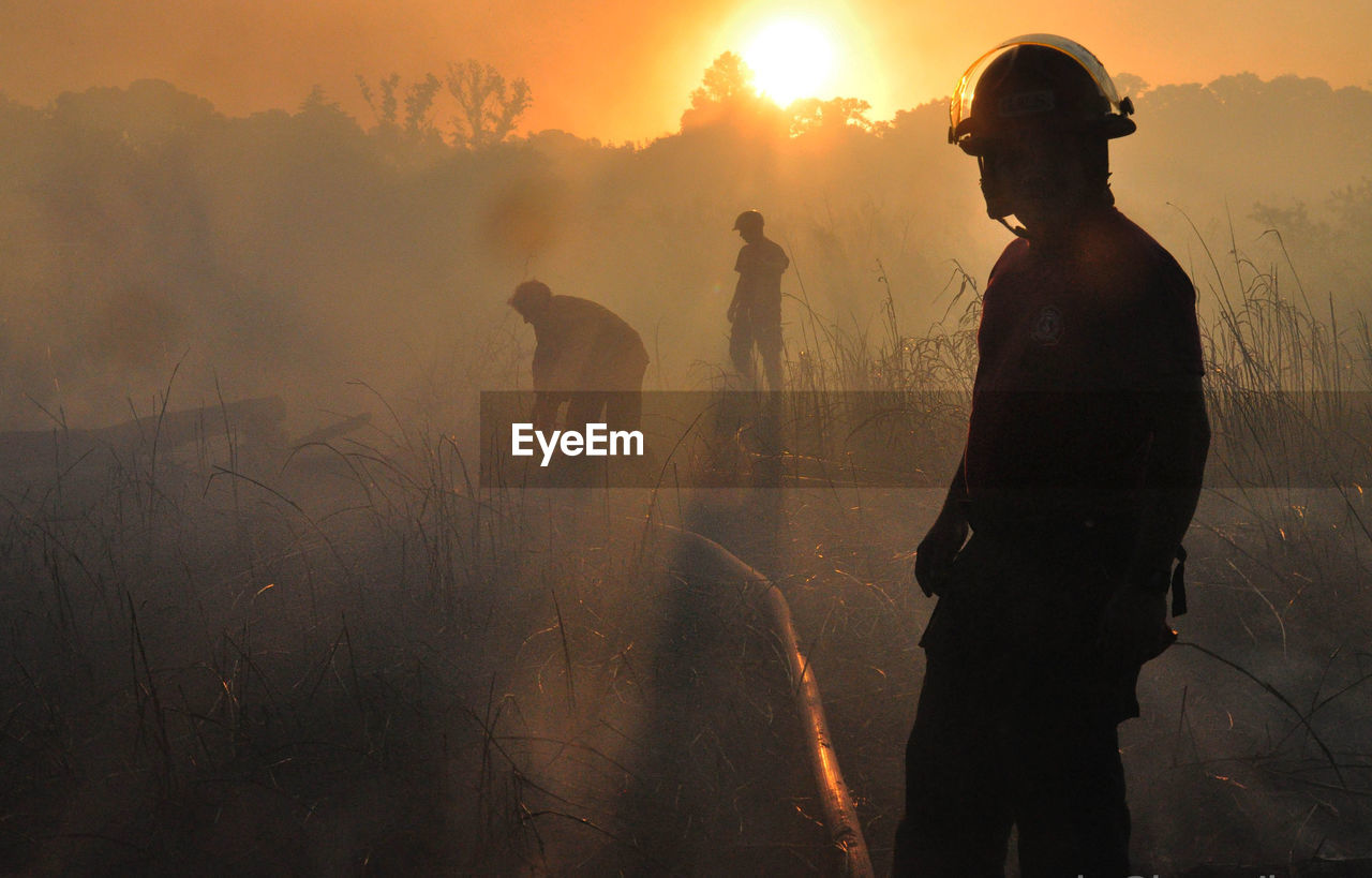 Men in protective workwear standing on field during sunset
