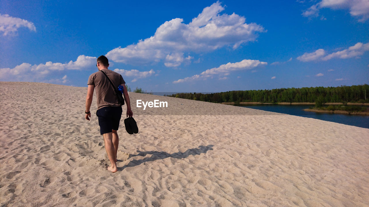 Rear view of man walking on sand at beach against sky