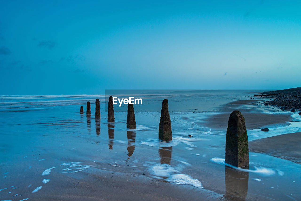 WOODEN POSTS IN SEA AGAINST SKY