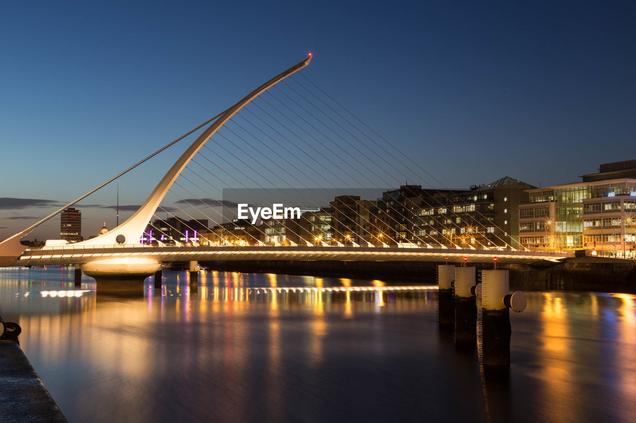 Illuminated samuel beckett bridge over river against sky