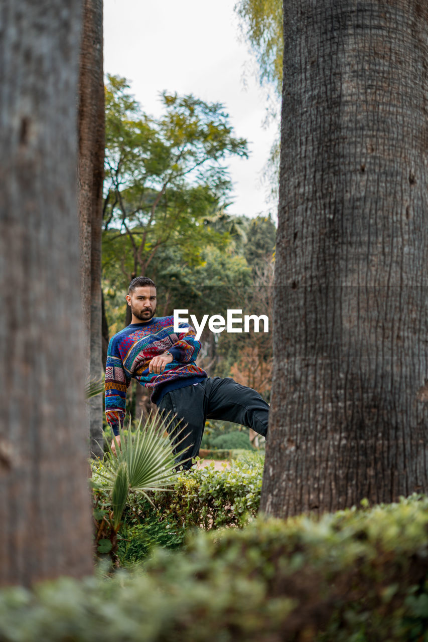 Caucasian model standing in between palm trees in a public park