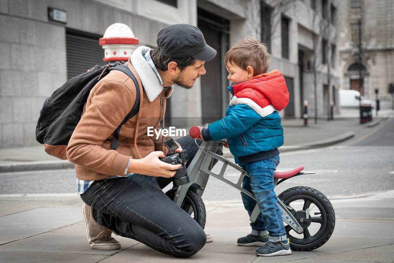 Full length of man holding camera with cute boy outdoors