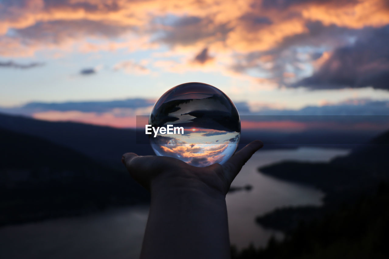 PERSON HOLDING CRYSTAL BALL AGAINST SUNSET SKY