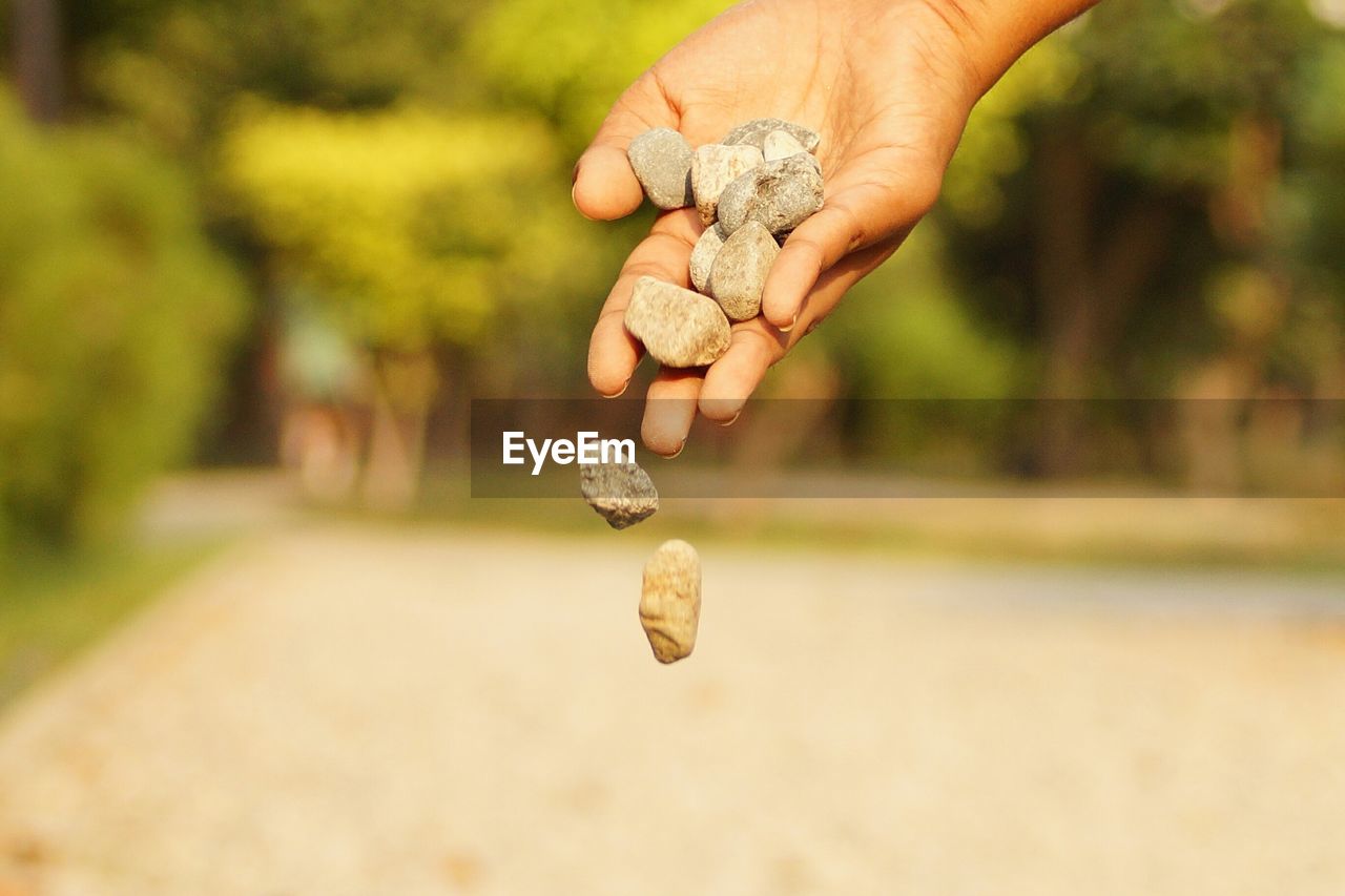 Cropped image of hand throwing stones on field