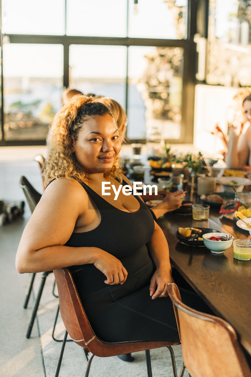Portrait of smiling plus size woman sitting on chair with breakfast at dining table