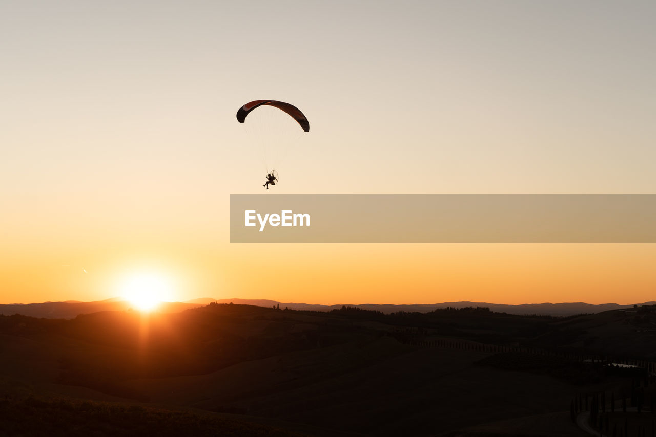 SILHOUETTE PERSON PARAGLIDING AGAINST SUNSET