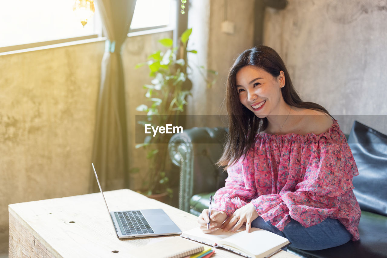 Smiling businesswoman looking away while writing in diary