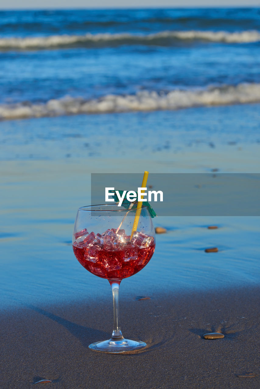 A cocktail with ice perched on the sand of the beach