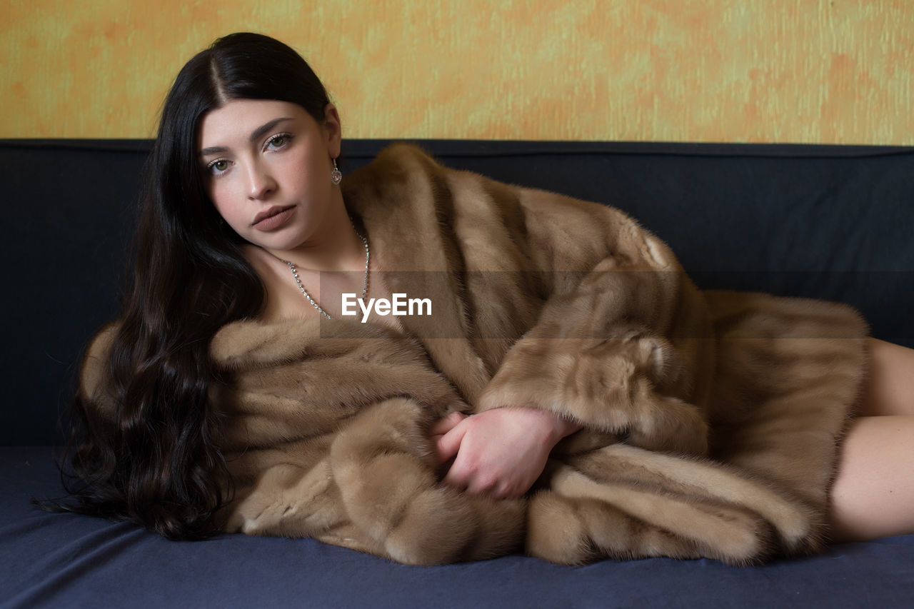 PORTRAIT OF BEAUTIFUL WOMAN SITTING ON SOFA AT HOME