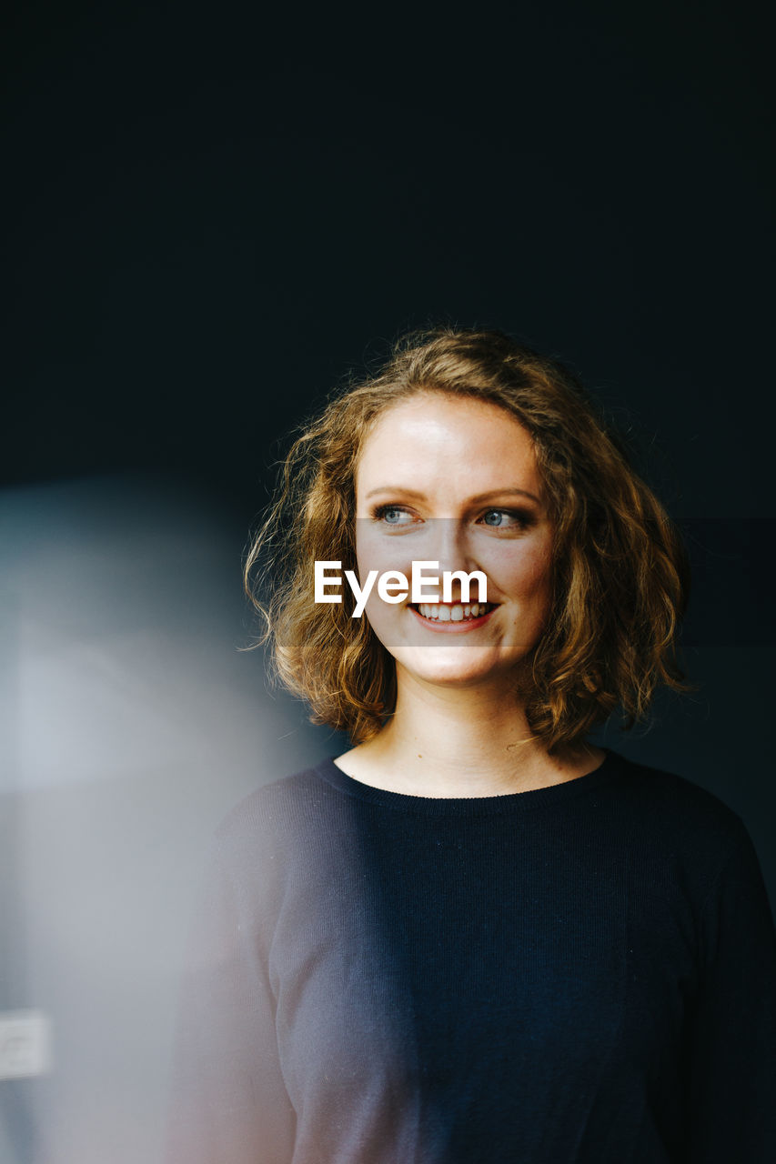 Portrait of a smiling young woman against black background 