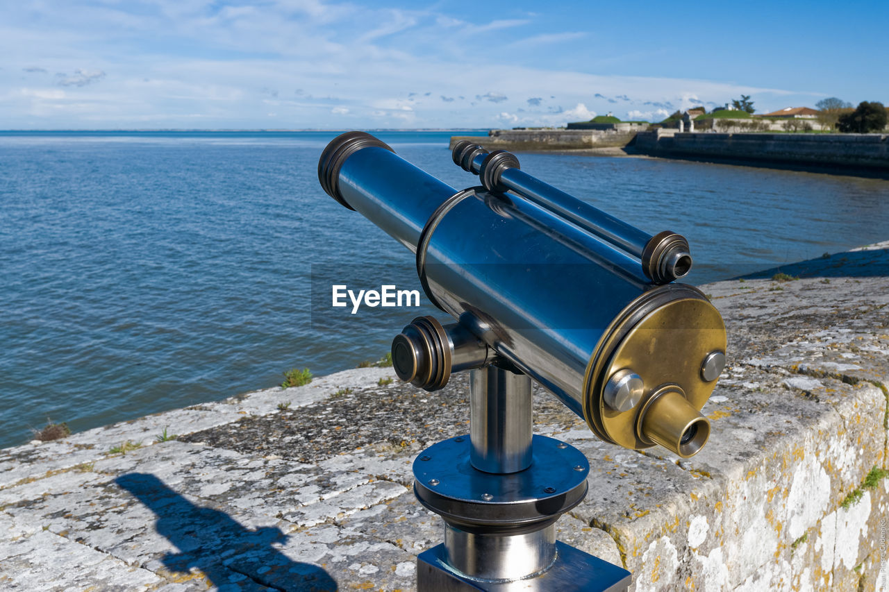 Coin-operated binocular by sea against sky