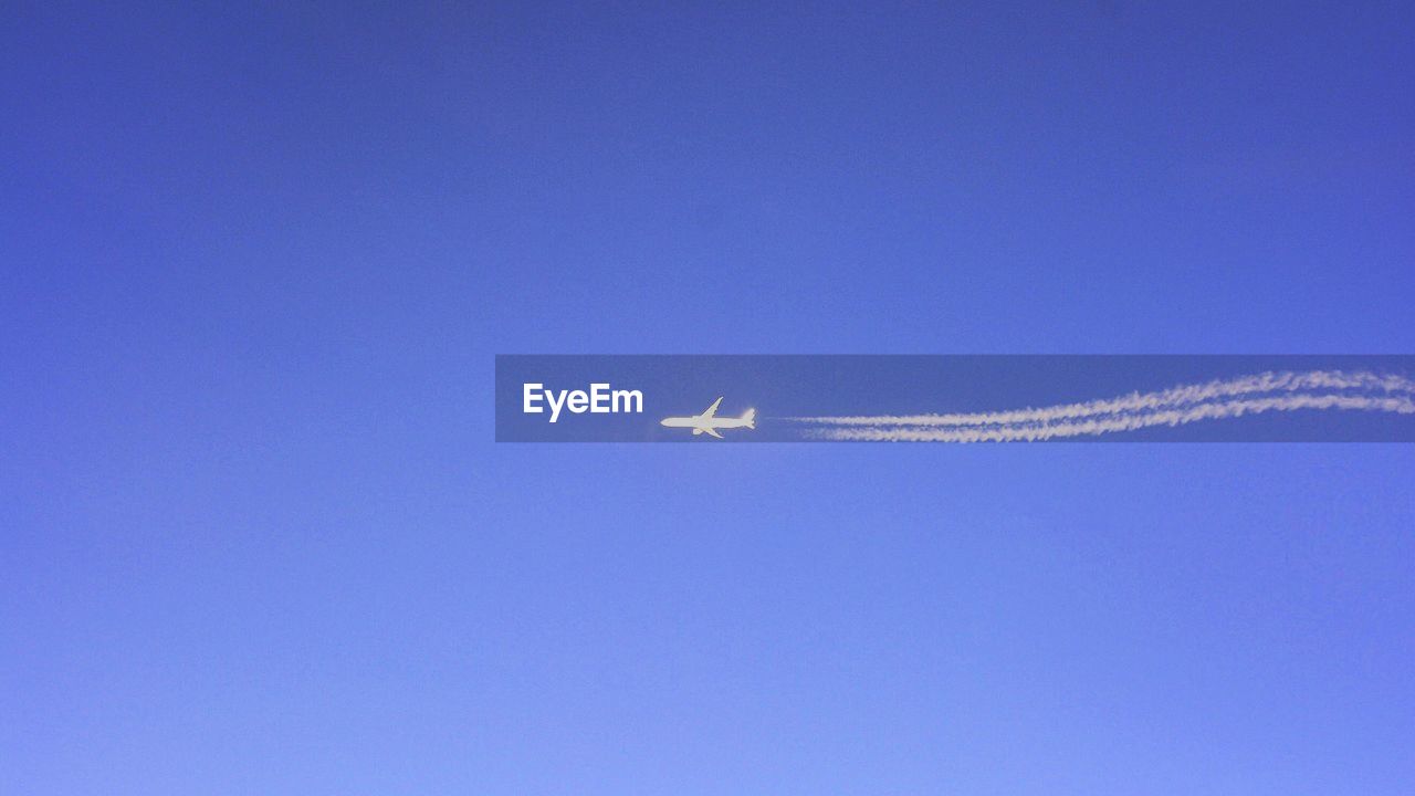 Low angle view of airplane flying against clear blue sky