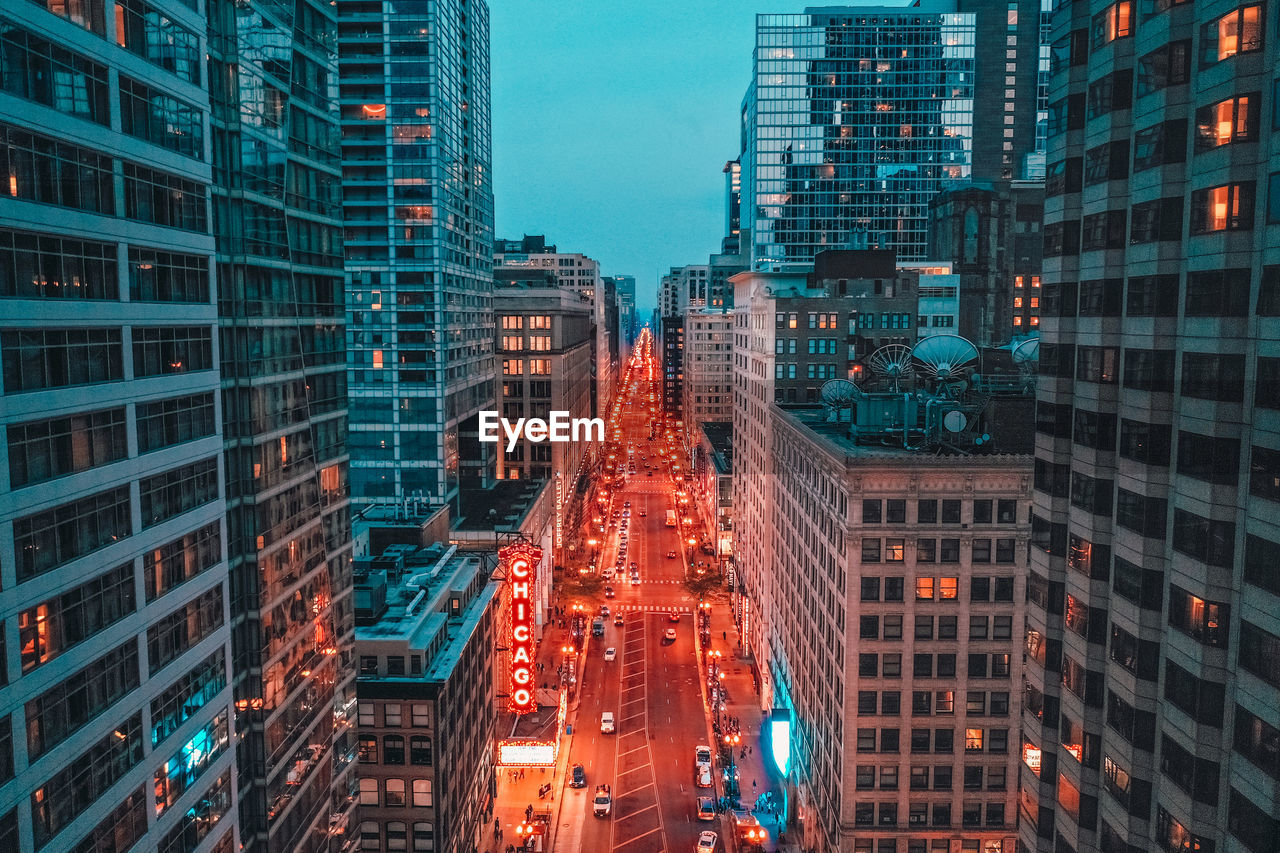 High angle view of vehicles on illuminated street amidst buildings in city at dusk