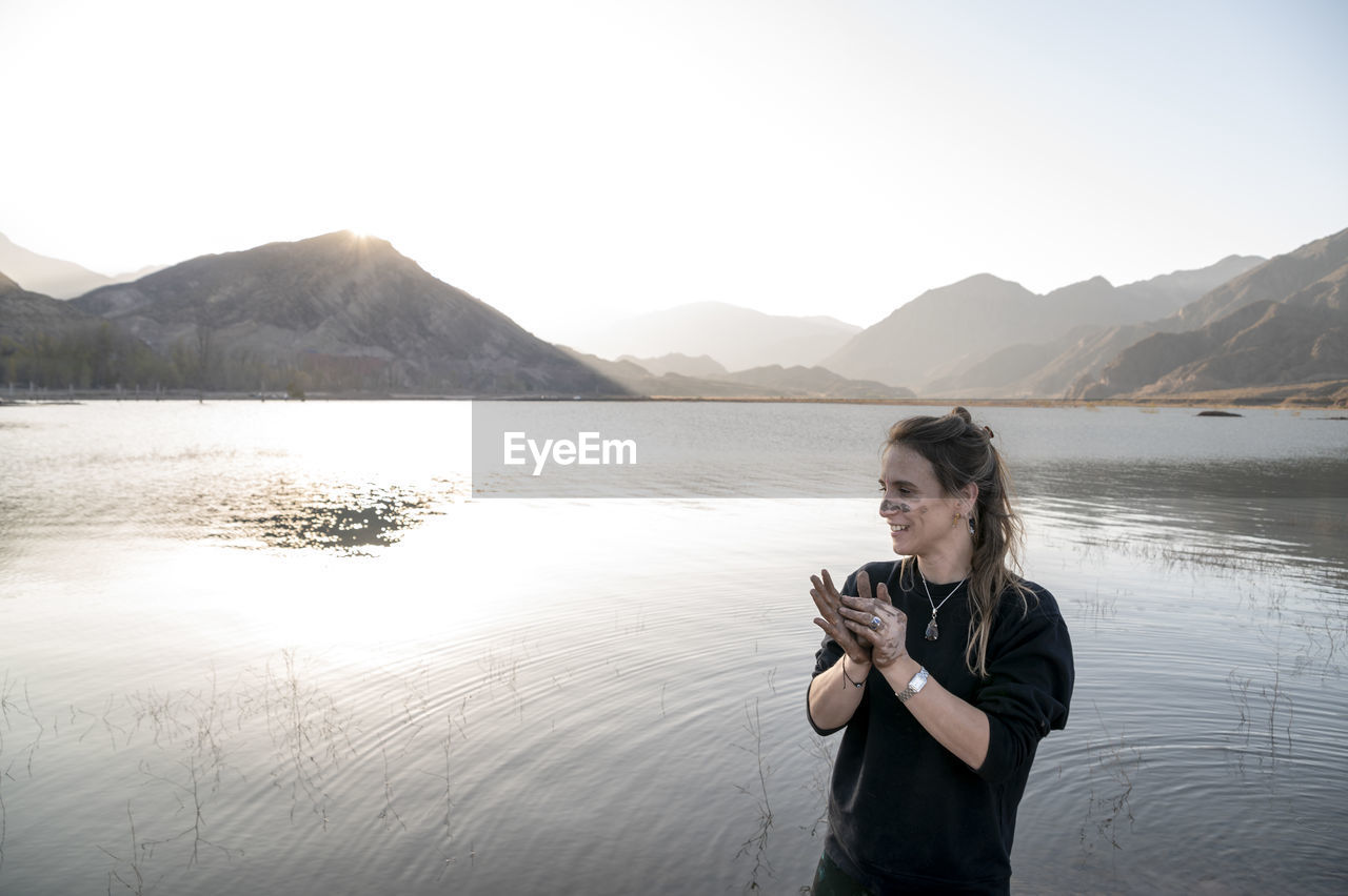 Woman putting mud on hands and face while enjoying outdoors in nature.