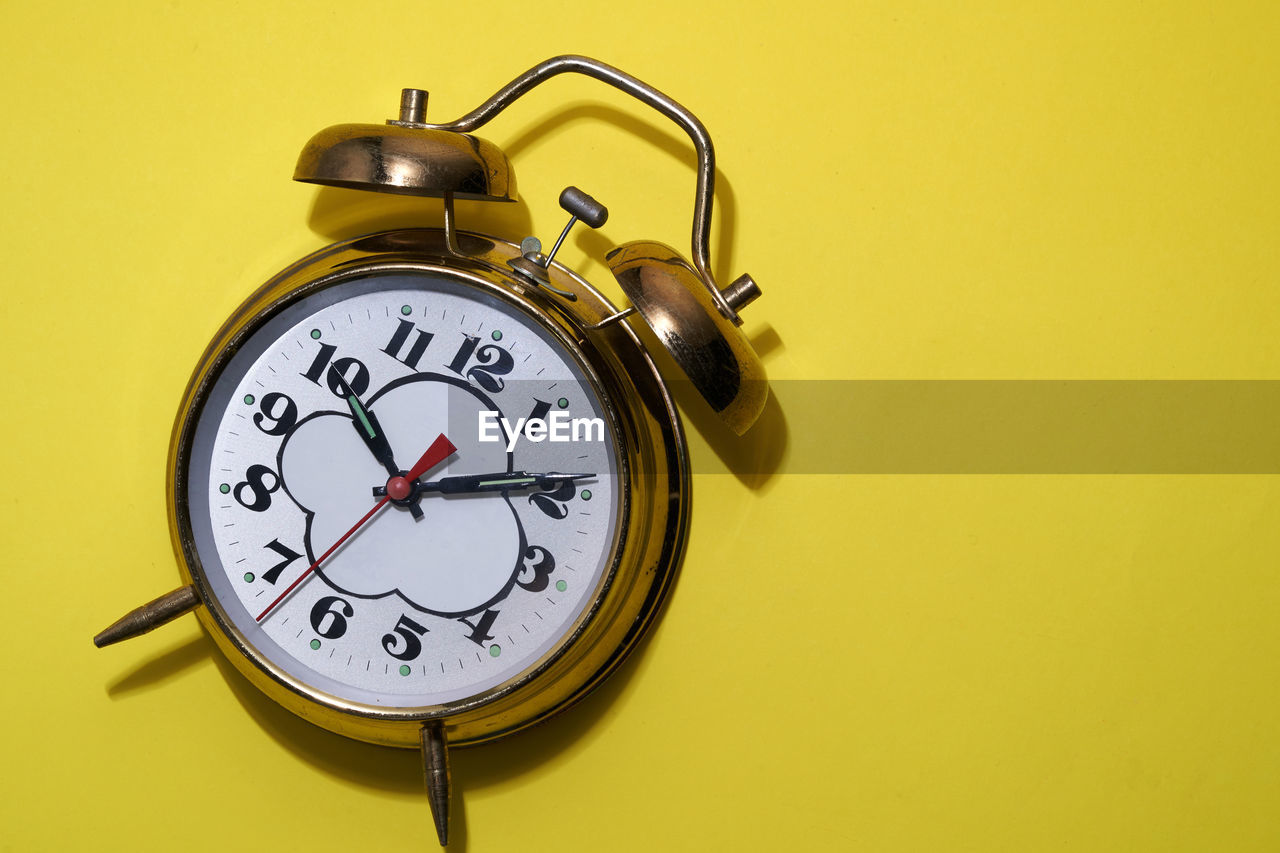 Gold colored alarm clock on yellow background