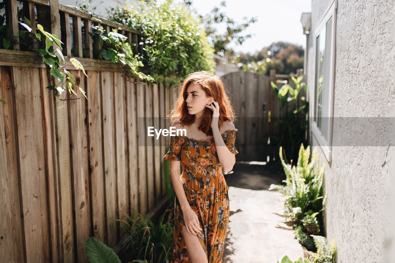 Young woman looking away while standing by house