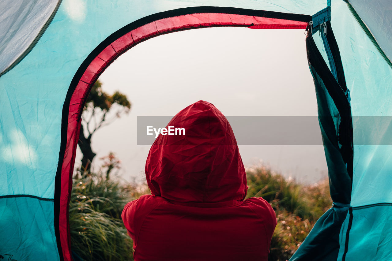 Rear view of person relaxing in tent on field