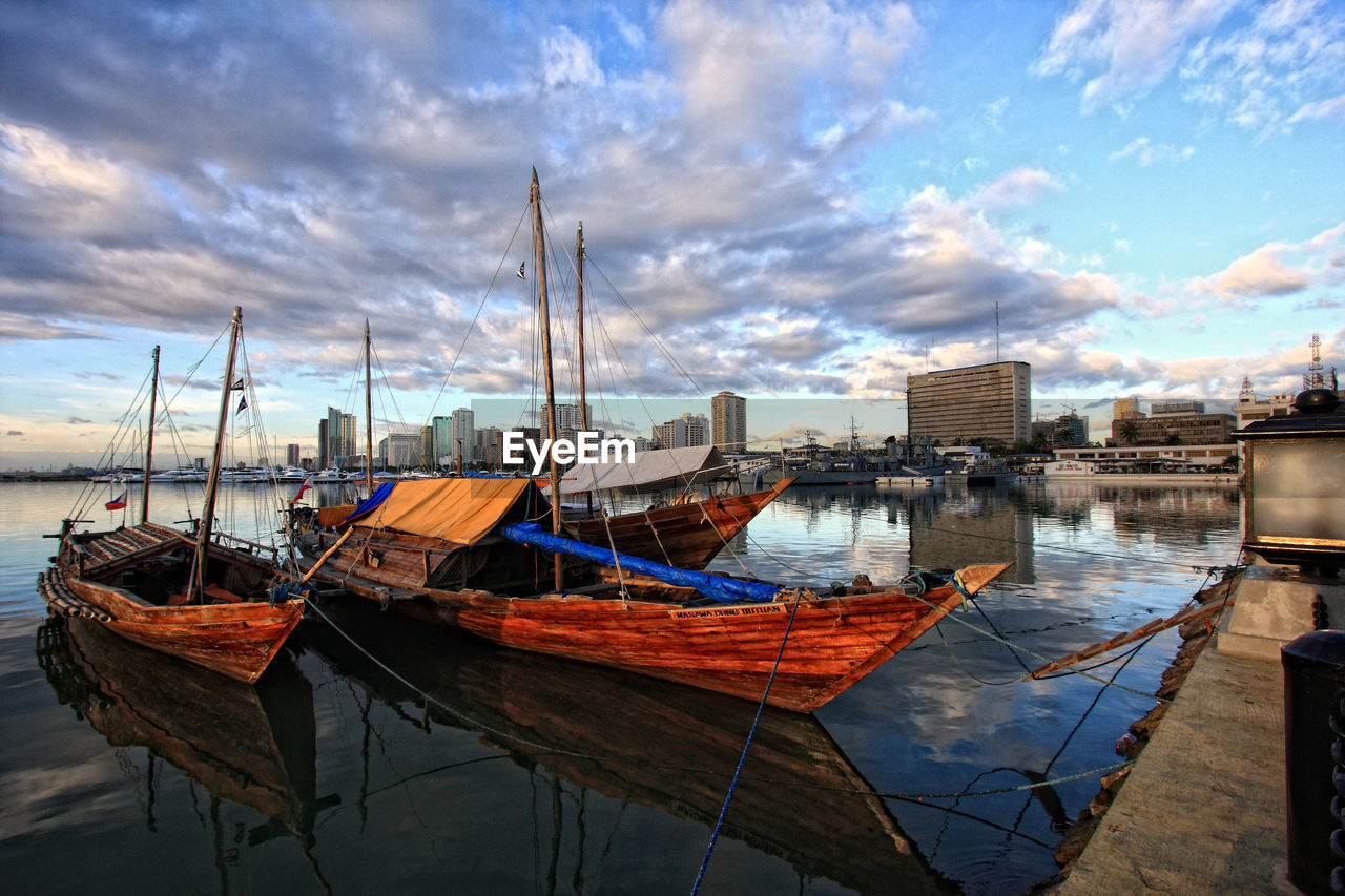 Boats moored on river in city against cloudy sky