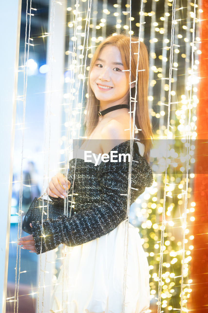 portrait of young woman looking away while standing against christmas tree