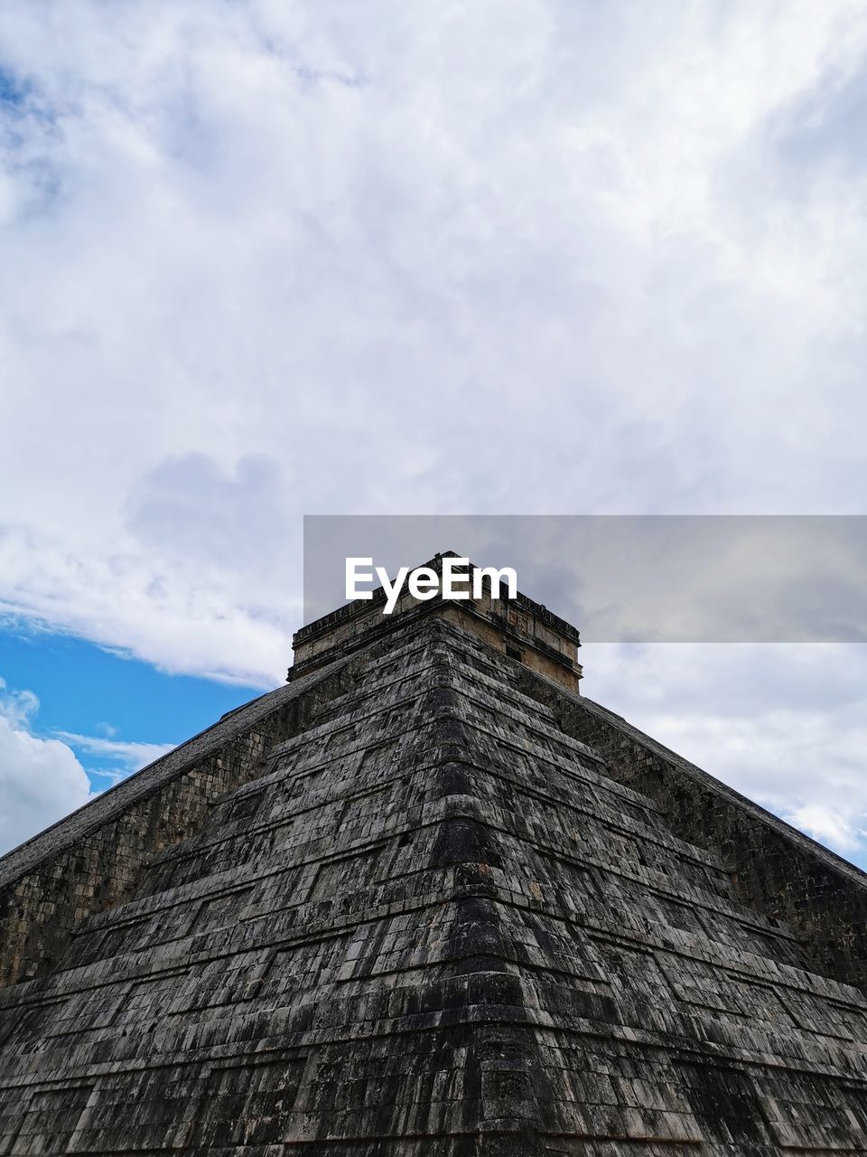 Low angle view of temple of kukulkan against cloudy sky