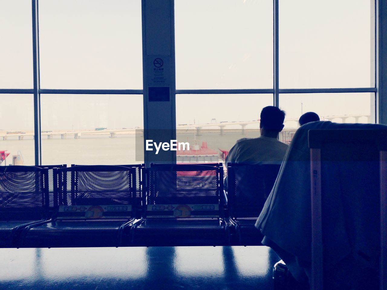 REAR VIEW OF MAN SITTING AT AIRPORT RUNWAY