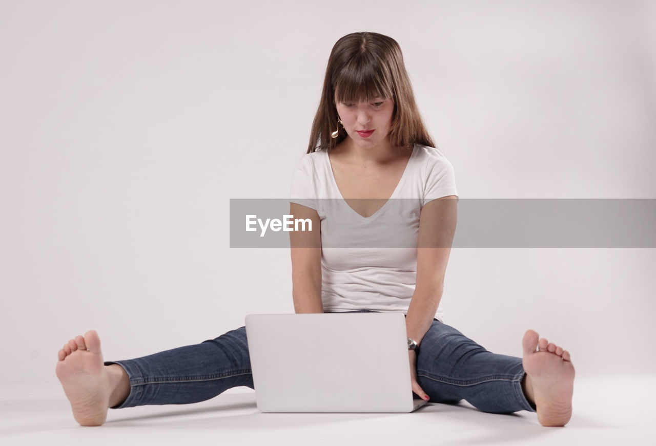 Young woman using laptop while sitting against white background