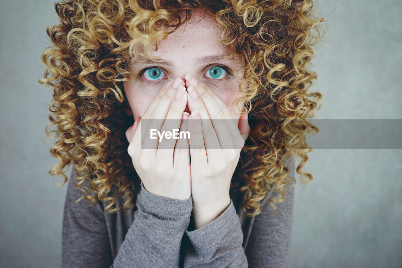 Portrait of young woman covering mouth with hands