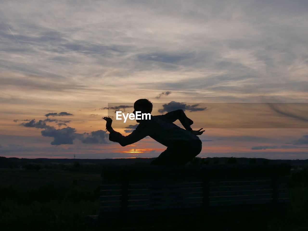 Playful man posing on bench against sky during sunset