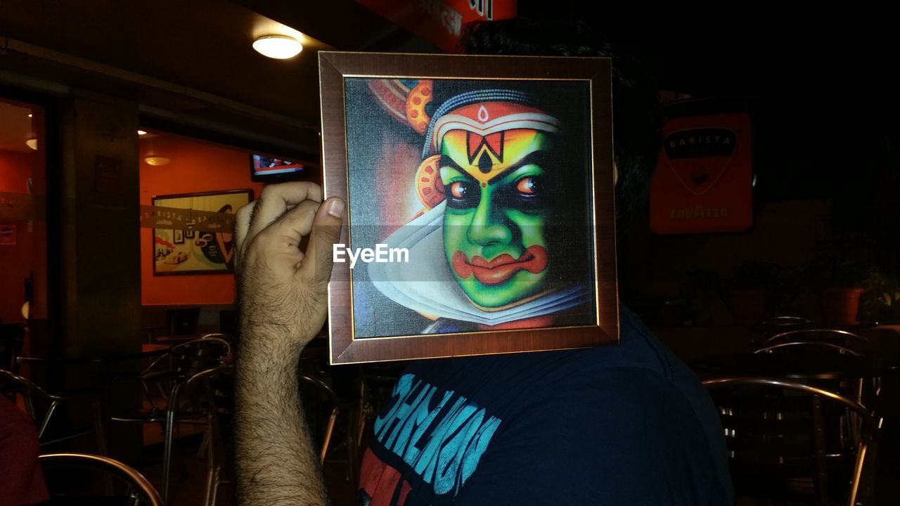 Man holding picture of kathakali dancer in front of his face