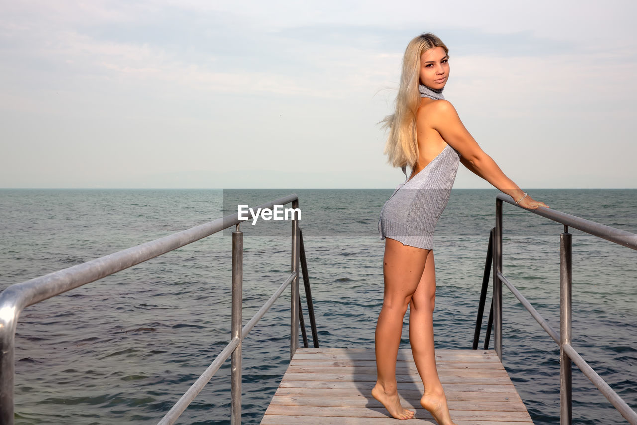 Side view of young woman standing on pier over sea against sky