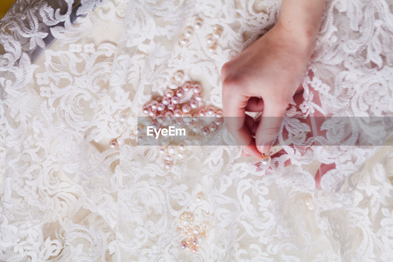 Cropped hand of woman stitching pearls on white wedding dress