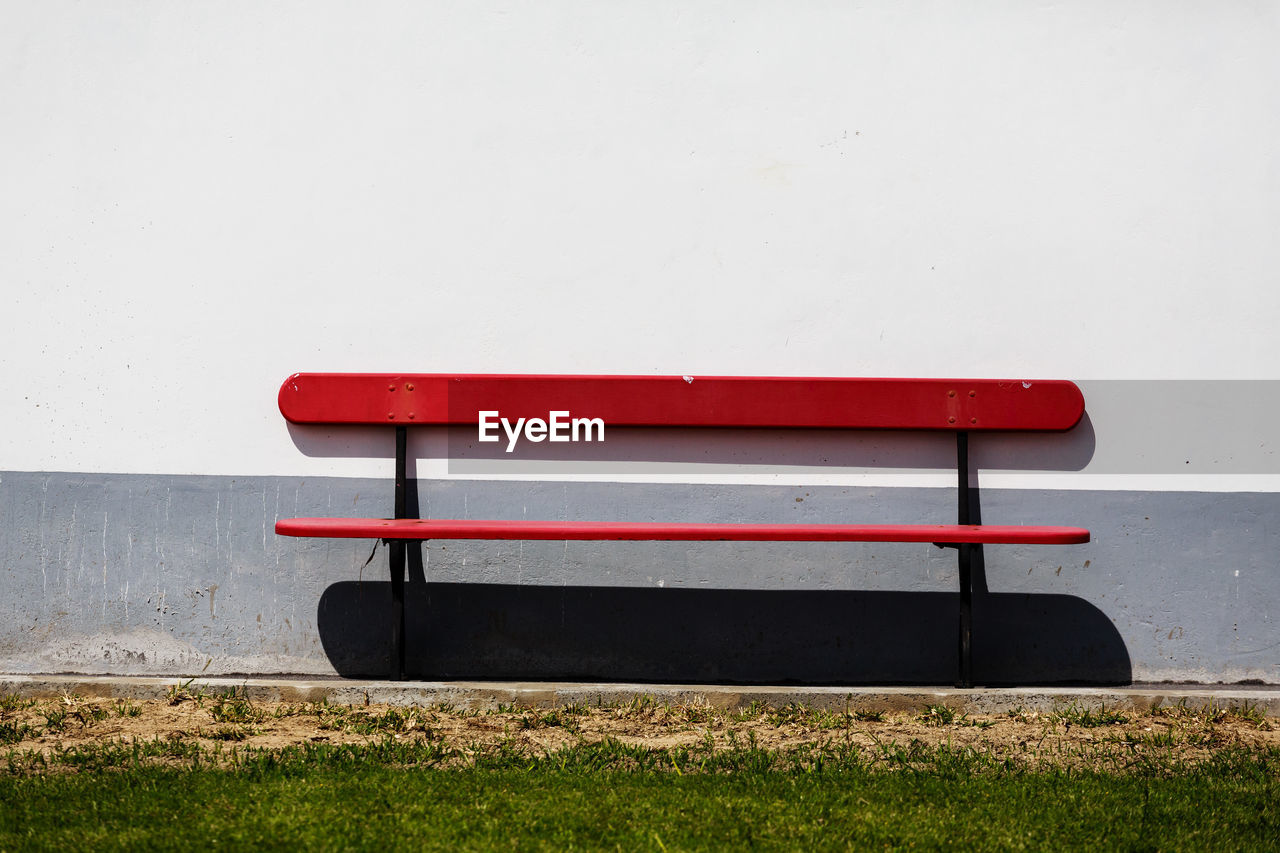 Empty bench on field against wall