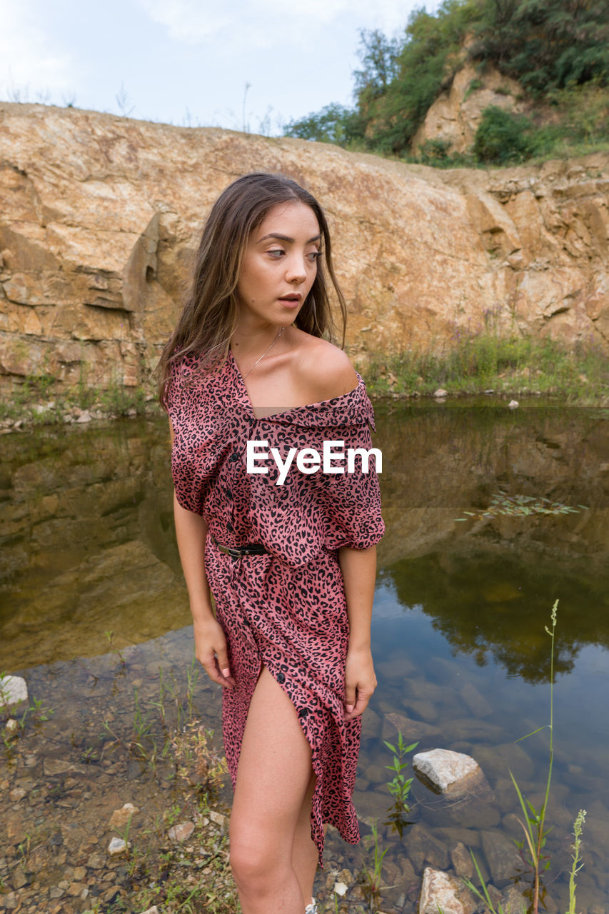 Portrait of beautiful young woman standing against water