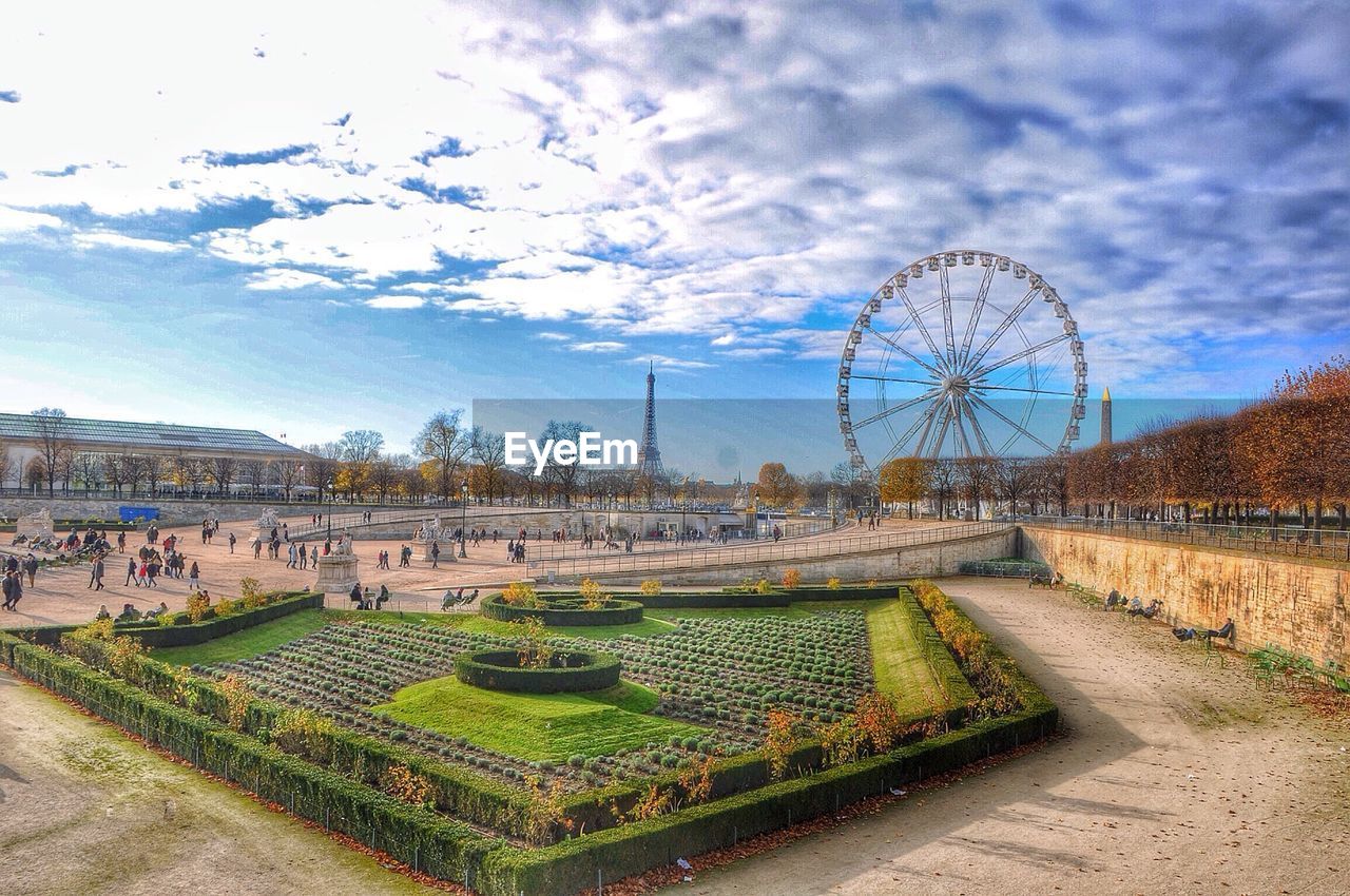 Ferris wheel with eiffel tower in background against cloudy sky