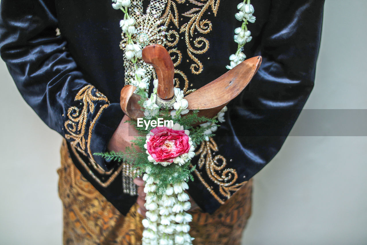 Midsection of in traditional clothing holding flowers standing against wall