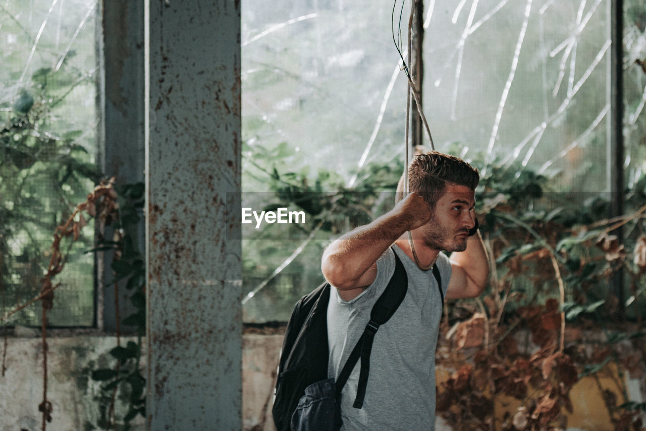 Young man holding rope standing against plants outdoors