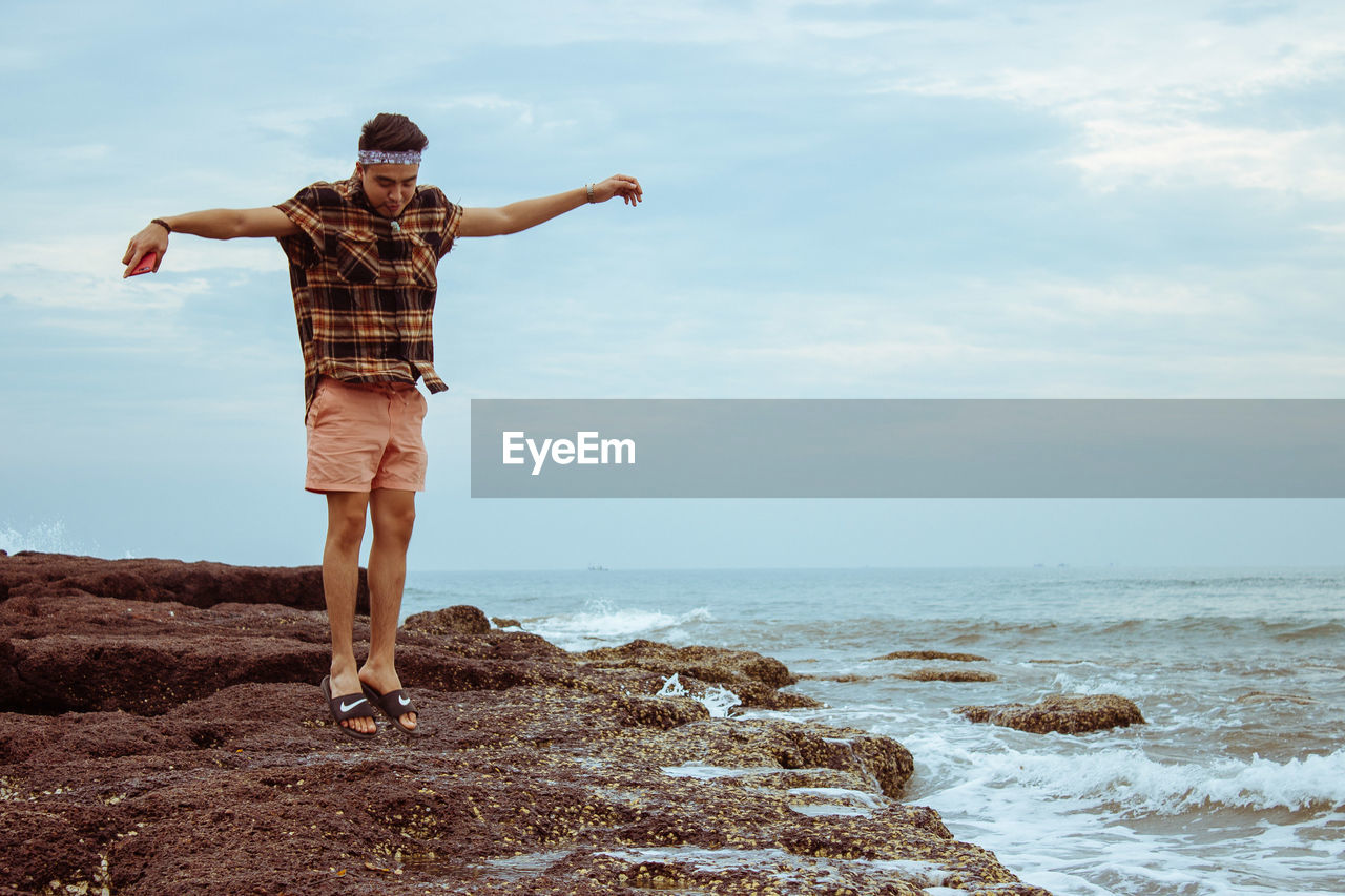 Rear view of man jumping on beach against sky