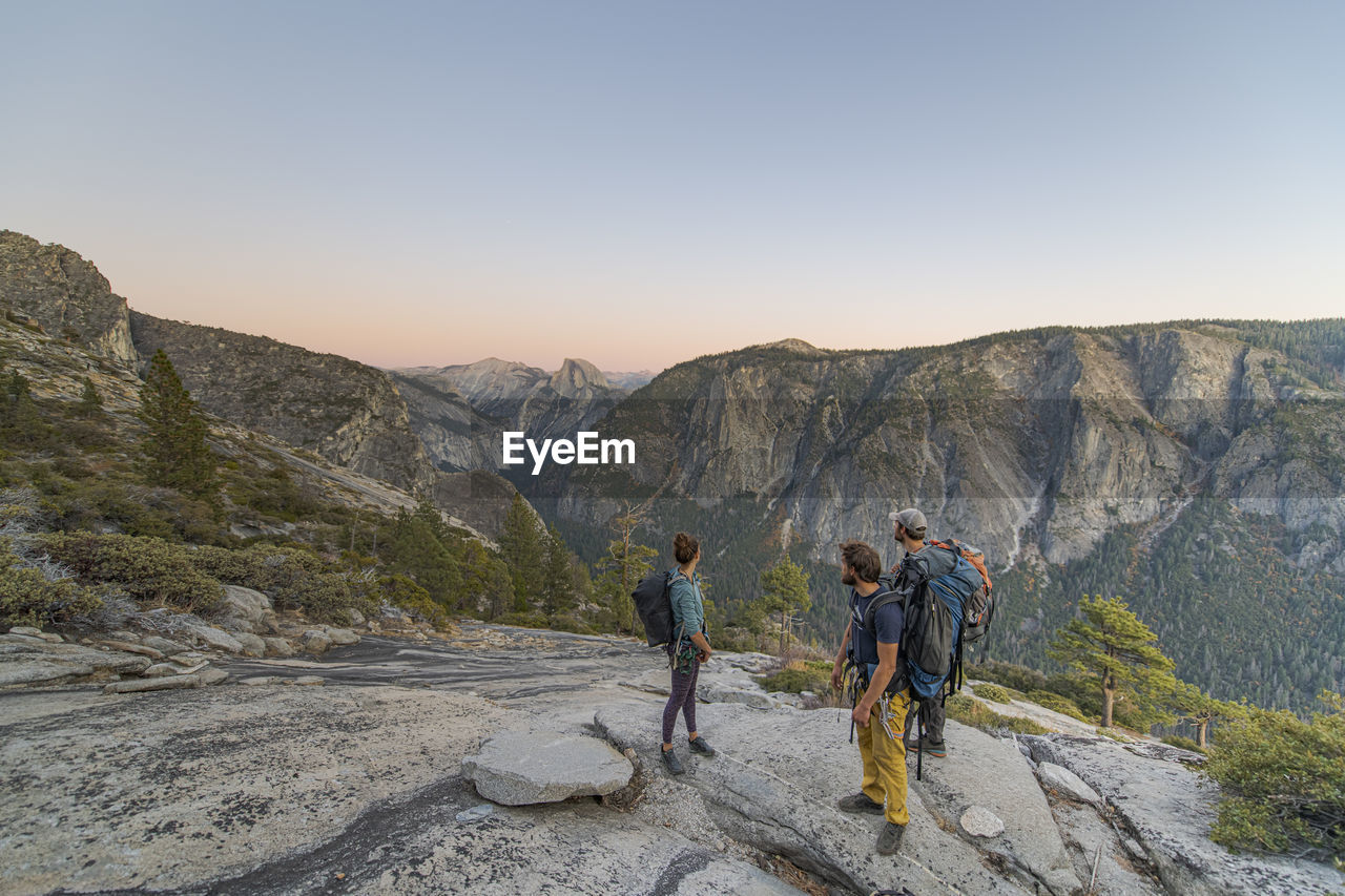 Three hikers looking at half dome from el capitan sunset yosemite