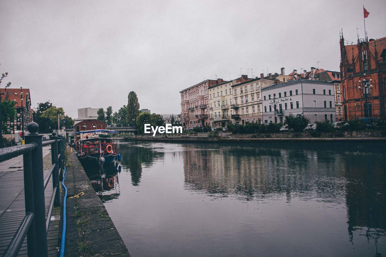 Buildings by river against sky in city