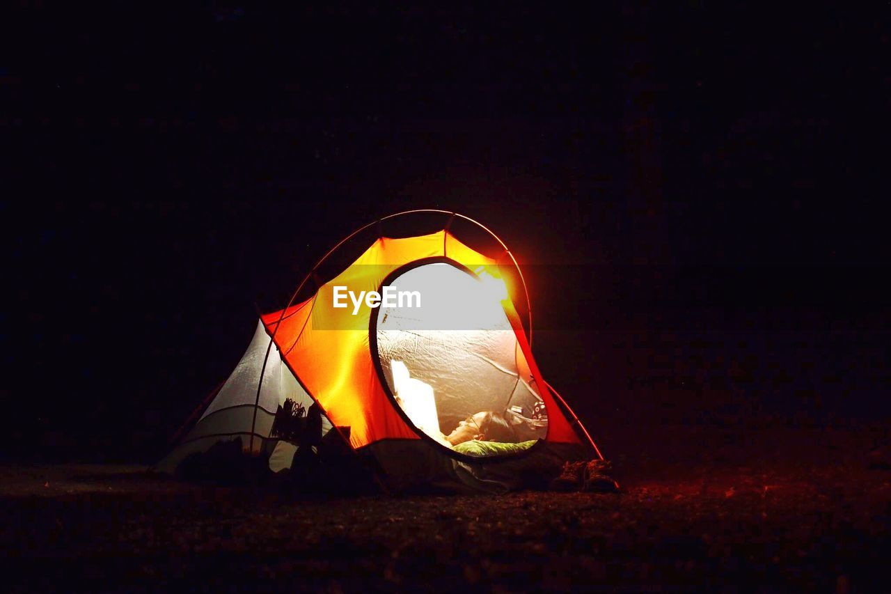 Woman lying in illuminated tent at night