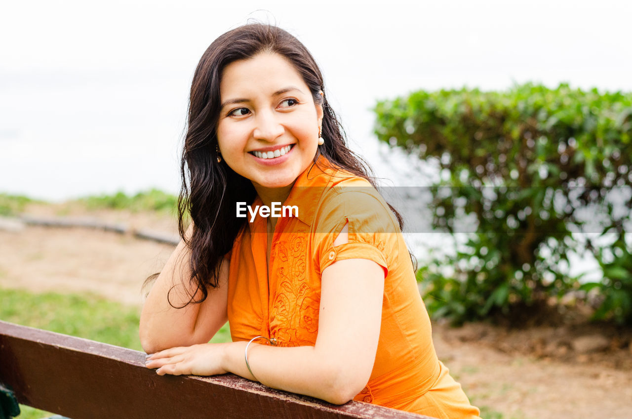 Smiling woman looking away while standing by railing outdoors